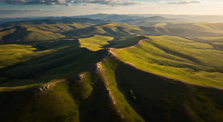 Aerial view of a dramatic mountain ridge cutting through vast, rolling green hills at golden hour.
