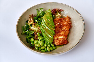 A visually appealing bowl featuring crispy fried fish paired with vibrant leafy greens, sliced avocado, and fresh edamame for a delicious and healthy meal.