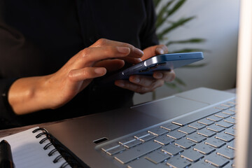 Close-up of the hands of a businesswoman sitting in front of her computer while holding a cell phone