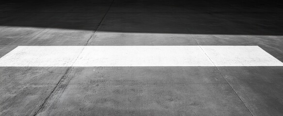 Minimalist monochrome image of a white line on textured concrete pavement in shadow and light contrast