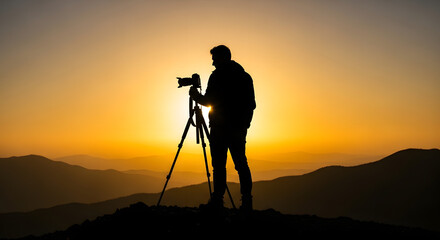 Silhouette of a photographer standing on a hilltop with a camera on a tripod, capturing the golden sunset over a mountainous landscape.