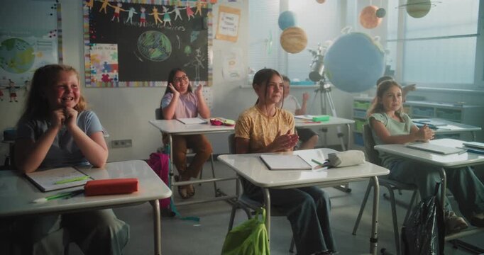 Cheerful Diverse Kids Sitting at Desks, Clapping Their Hands, Interacting with Teacher During Dynamic Gamified Activity. Female Teacher Providing Interactive Lesson to Elementary School Students.