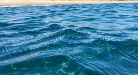 Fototapeta premium Close-up view of clear, blue water with gentle ripples and a distant sandy beach.