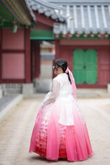 Fototapeta premium In Seoul in June 2025, two Korean women in their twenties wearing pink and sky-blue hanbok stand in front of the traditional brick gate of Gyeongbokgung Palace, their poise echoing ancient grace.