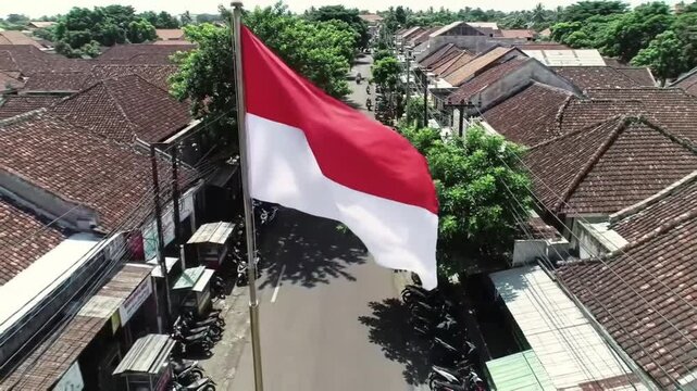 The red and white Indonesian national flag waving proudly above a traditional urban neighborhood.