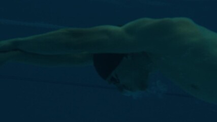 Professional swimmer trains in the pool, underwater view. Male swimmer dives and swims fast during swimming work out in the empty morning pool