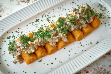Deliciously Baked Potato Croquettes Topped with Creamy Mushroom Sauce and Fresh Herbs on a White...