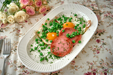 A Delectable Dish Featuring Fried Eggs, Sliced Ham, Fresh Green Peas, and a Touch of Garnish on a Floral Table Setting