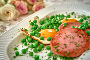 A colorful breakfast plate featuring fried eggs, sliced meat, and vibrant green peas garnished with herbs, complemented by a floral background.