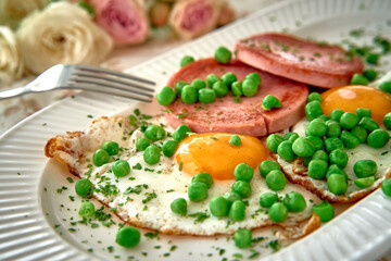 Delicious Breakfast Platter Featuring Sunny-Side-Up Eggs, Sliced Ham, and Fresh Green Peas Layered on a Decorative Plate Surrounded by Beautiful Blooms
