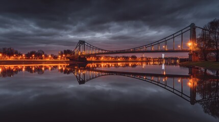Obraz premium A suspension bridge spans calm waters at twilight, illuminated by warm streetlights with reflections on the surface,