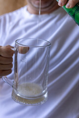 man pouring beer into glass mug in front of white t-shirt