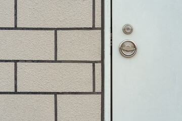 Close-up of a modern white door with a silver metal handle and lock next to a textured grey brick wall, showing detail and contrast.