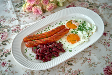 Delicious Breakfast Plate Featuring Cooked Eggs, Sizzling Sausages, and Flavorful Red Beans on a Floral Tablecloth