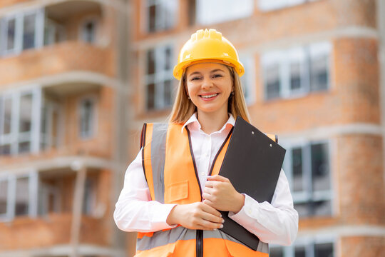 Smiling female architect on construction site with clipboard and safety gear