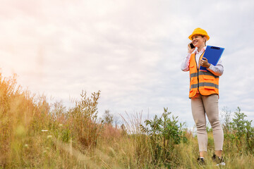 Female construction worker on mobile phone with clipboard in field