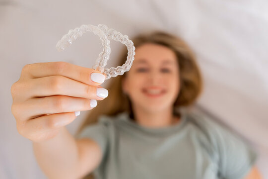 Smiling woman holding clear orthodontic aligners for teeth alignment and correction