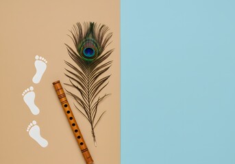 Krishna janmashtami photo of a peacock feather and a flute are placed next to baby footprints on a split background of beige and blue, evoking the divine presence and playful nature of lord krishna kr