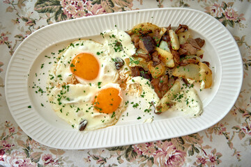 A Delicious Plate of Fried Eggs and Sautéed Potatoes with Fresh Herbs on a Floral Tablecloth for a Perfect Breakfast Experience