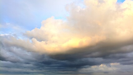 Obraz premium Dramatic cloudy sky with soft golden sunlight breaking through layers of thick evening clouds