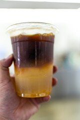 Ice yuzu black coffee in plastic cup on hand.