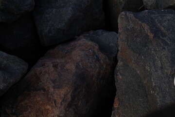 Rocks in various shades of gray and brown are clustered together, showcasing a mix of textures and colors, illuminated by soft, fading light.