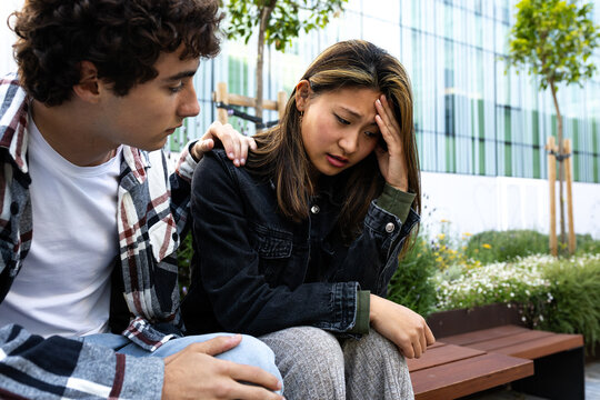 Young man comforting sad asian woman sitting outdoors