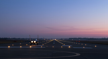 Fighter jet preparing for takeoff at dusk with runway lights creating a line