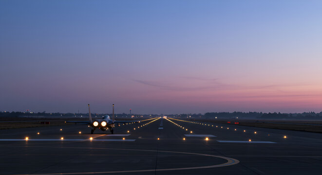 Fighter jet preparing for takeoff at dusk with runway lights creating a line - Powered by Adobe