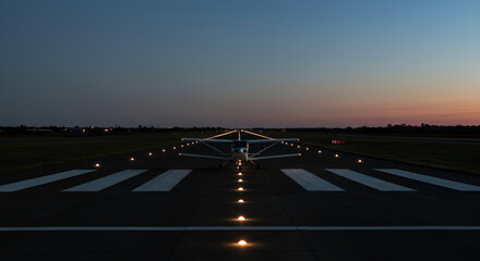 Small plane on runway at dusk, ready for takeoff with illuminated runway lights