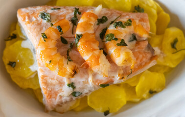 Salmon fillet cooked with shrimps and potatoes, seasoned with parsley, creating a healthy and delicious meal rich in omega-3 fatty acids, proteins, vitamins, and nutrients