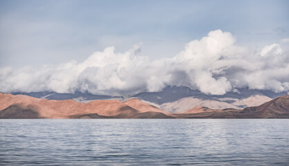 Panorama landscape of Lake Karakul in the Pamir mountains in the Tien Shan against the background of high snowy rocky peaks with clouds, morning panorama of the lake for the background