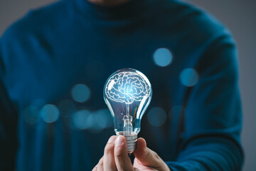 A person holds a light bulb with a brain illustration, symbolizing ideas, creativity, and...