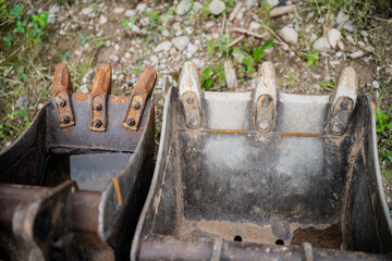 Two excavator buckets with visible teeth and worn metal surfaces placed on construction ground for machinery maintenance or equipment replacement context