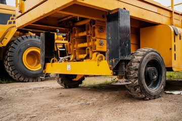 Close-up view of yellow scissor lift chassis and wheels on construction site showing mechanical components and heavy-duty industrial equipment