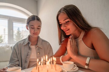 Birthday Cake Teenagers Home Celebration: Two teenage girls celebrate a birthday with a cake and candles indoors, expressing wishes.