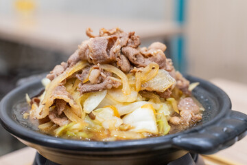 A traditional Asian clay pot rice dish is served piping hot, nestled in a rustic earthenware pot. Steam rises from the sizzling surface, revealing layers of tender sliced meat, crisp bean sprouts