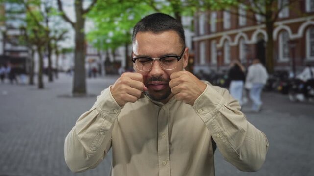 Man grabbing face with fingers on street in a mocking crying gesture wearing glasses under green tree canopy; mockery.