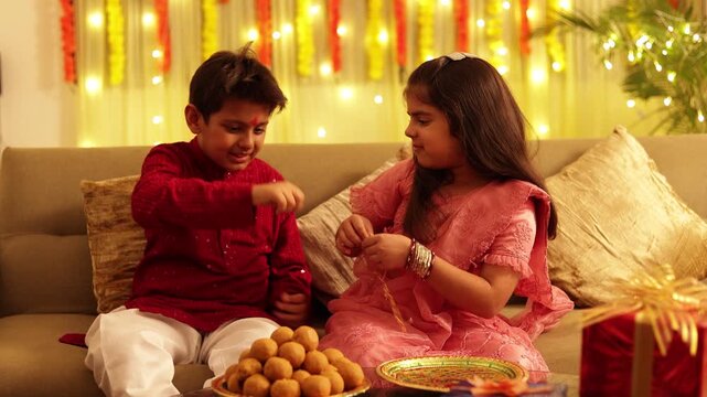  Happy Indian Brother and Sister Kids Celebrating Raksha Bandhan Festival together. Tying  Rakhi and Enjoying Ladoo Sweets. Culture Of India. 4k