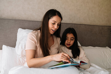 The mother reads a story to her daughter in bed and they are sharing a moment together.