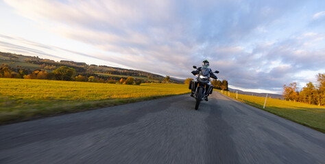 Driver riding motorcycle on empty road during sunset, autumn mountains