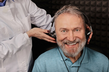 Hearing loss treatment. Positive senior man wearing audiometry headphones while hearing test and...
