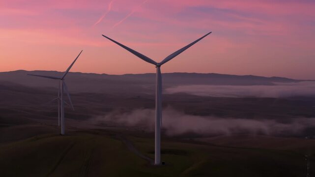 Wind turbines stand tall on rolling hills, generating clean energy at sunrise in Altamont Pass, Livermore, California, USA. The pink sky reflects the promise of a sustainable future.