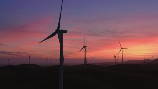 Wind turbines stand silhouetted against a vibrant sunset sky in Altamont Pass, Livermore, California, USA. These turbines convert wind energy into electricity, promoting renewable energy.