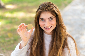 Young pretty caucasian woman holding a Bitcoin at outdoors smiling a lot