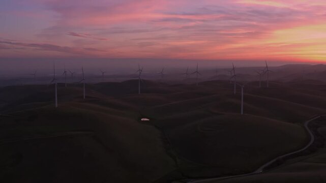 Wind turbines stand tall on rolling hills in Altamont Pass, Livermore, California, USA, at sunset. These windmills convert wind power into electricity, providing a clean energy source.