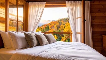 In the cabin, there is an open window with a wooden frame and white curtains. On one side of the window, you can see nature in autumn colors. The view from inside shows mountains covered in fog and tr