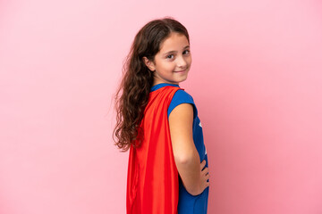 Little caucasian girl isolated on pink background in superhero costume and doingposing with arms at...