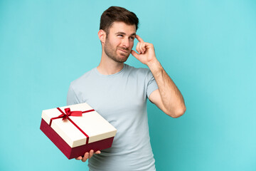 Young caucasian man holding a gift isolated on blue background having doubts and with confuse face...