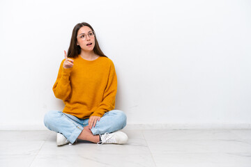 Young girl sitting on the floor isolated on white background thinking an idea pointing the finger up
